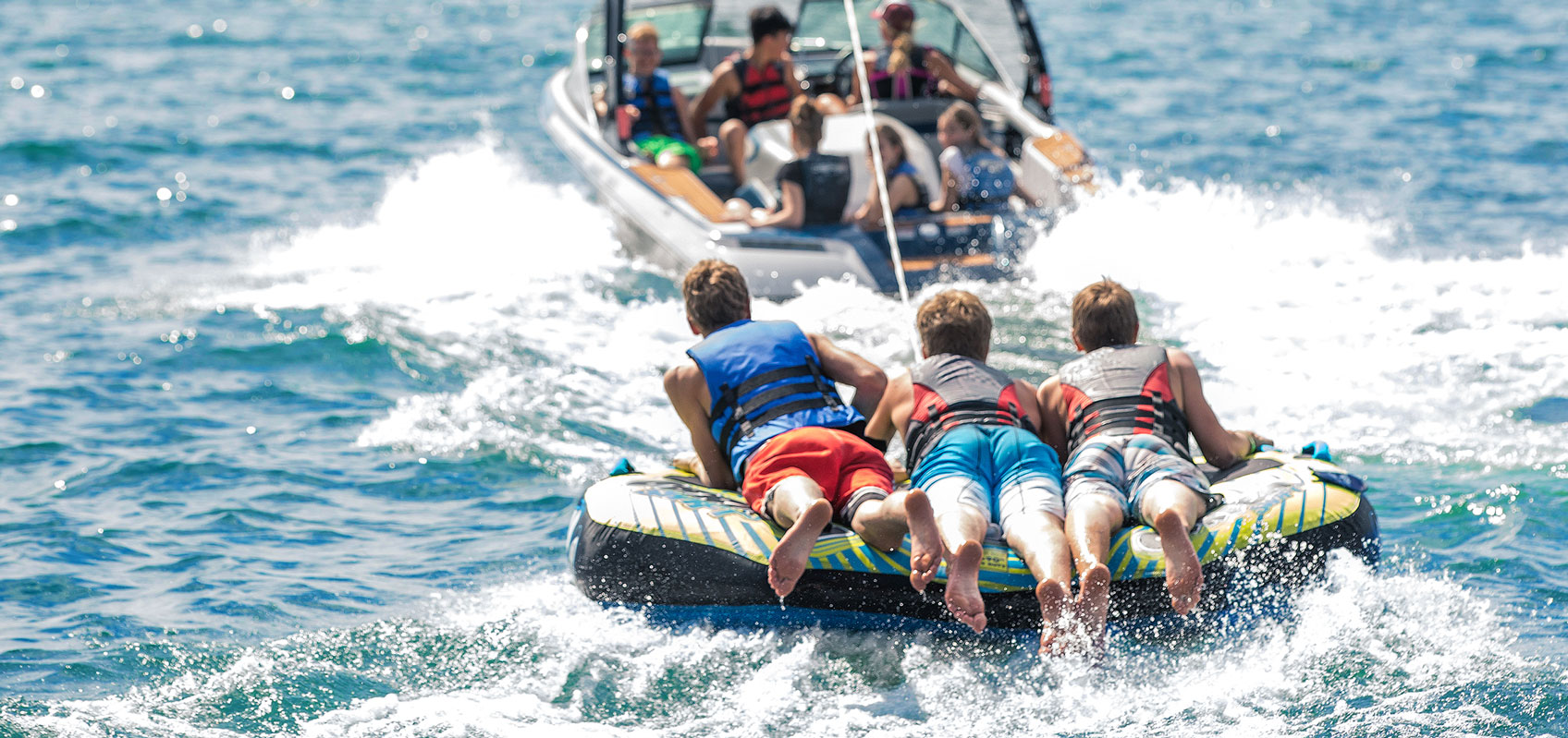 backside view of three boys on raft being pulled by speed boat