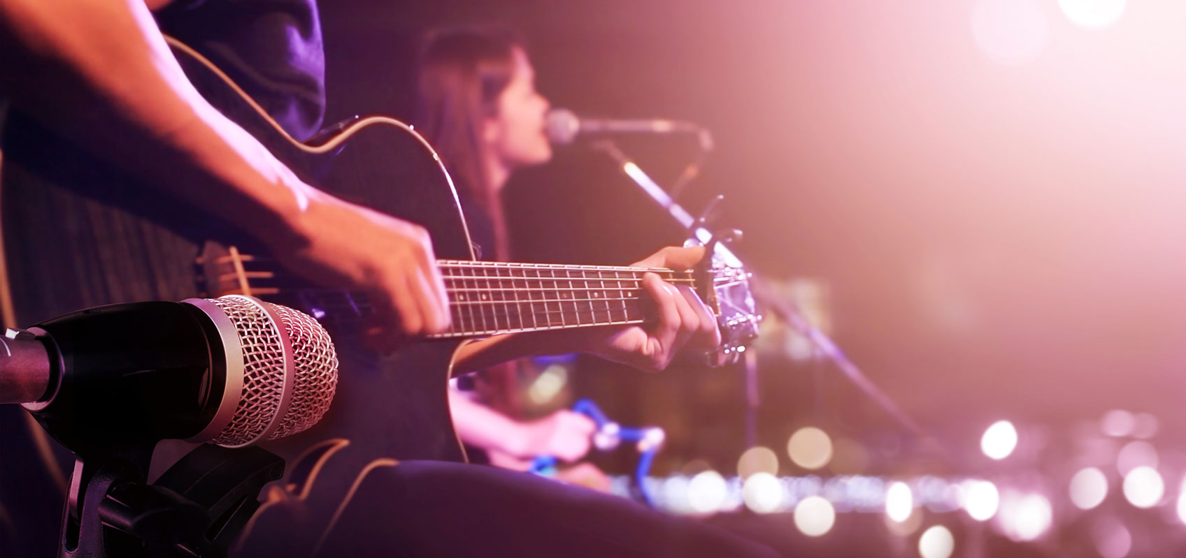 close up view of man playing guitar with woman singing into microphone in the background