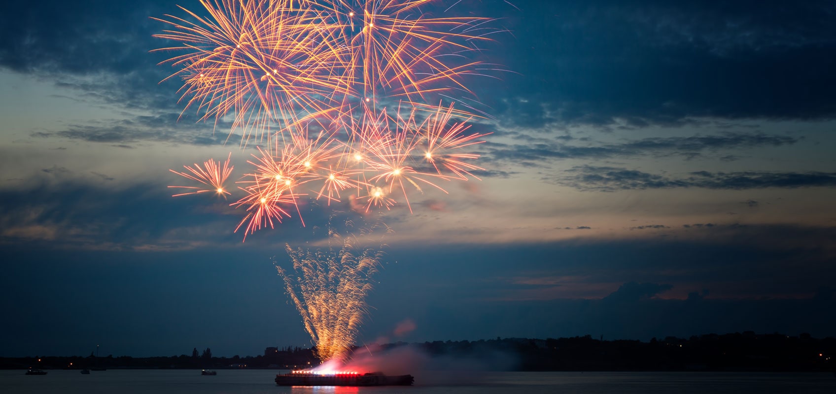red fireworks in the distance over a lake at dusk