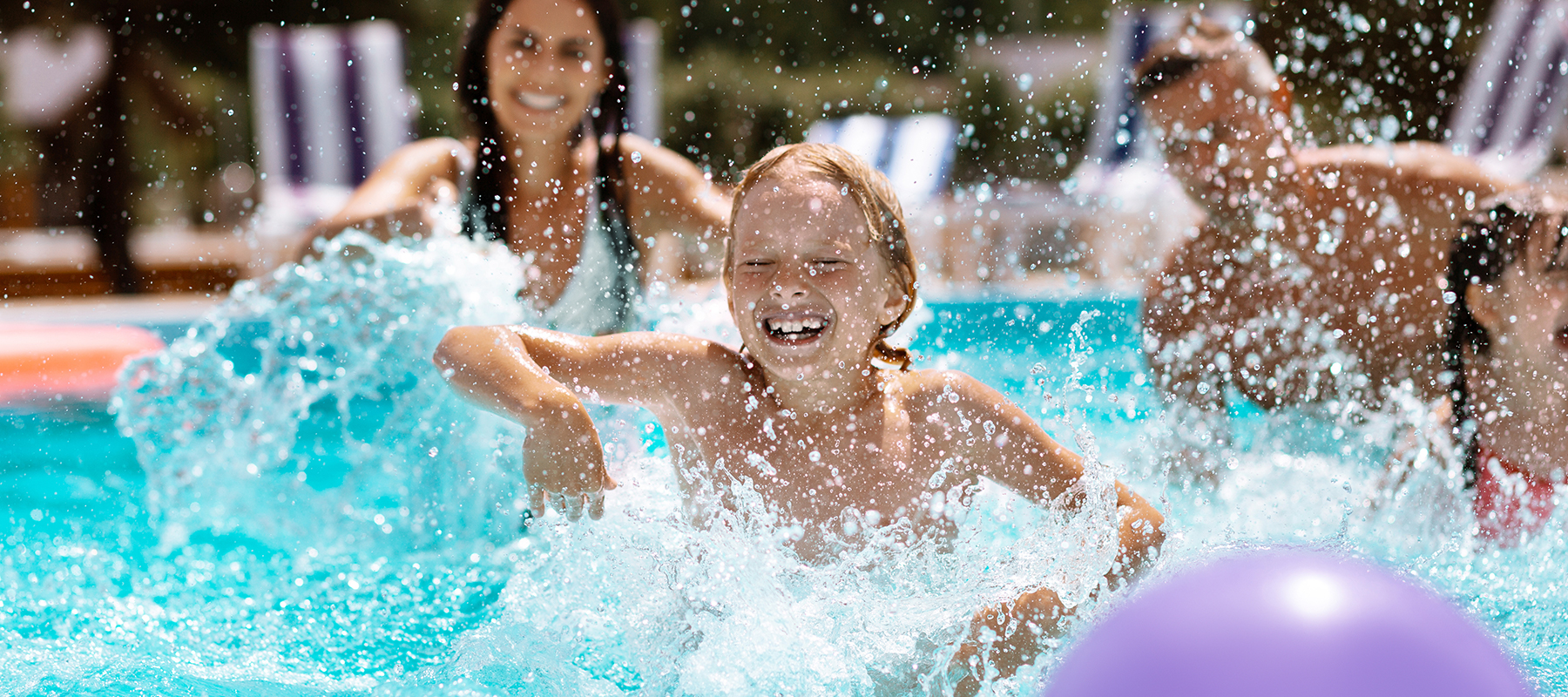 kid splashing water in swimming pool with family