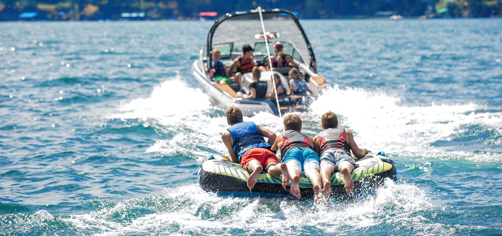 three boys enjoying riding a tube pulled by a boat on lakewater
