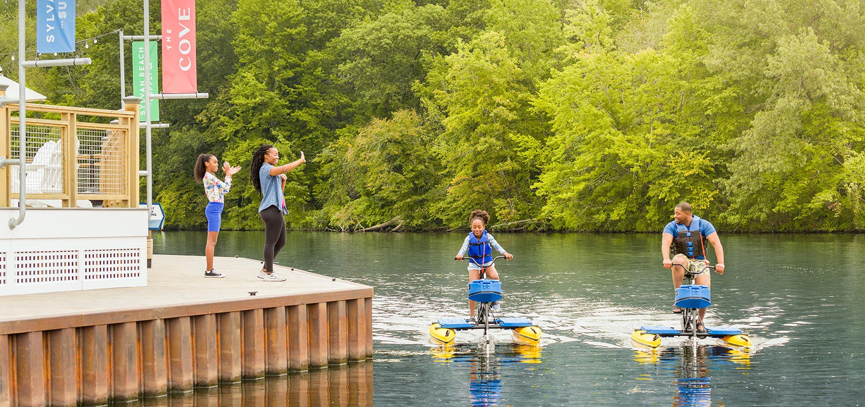 Mother and daughter wave as father and daughter ride by on waterbikes