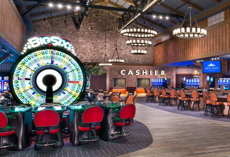 a bustling casino interior featuring a central roulette wheel, slot machines along the walls, a blackjack table in the foreground, and a cashier's cage in the background.