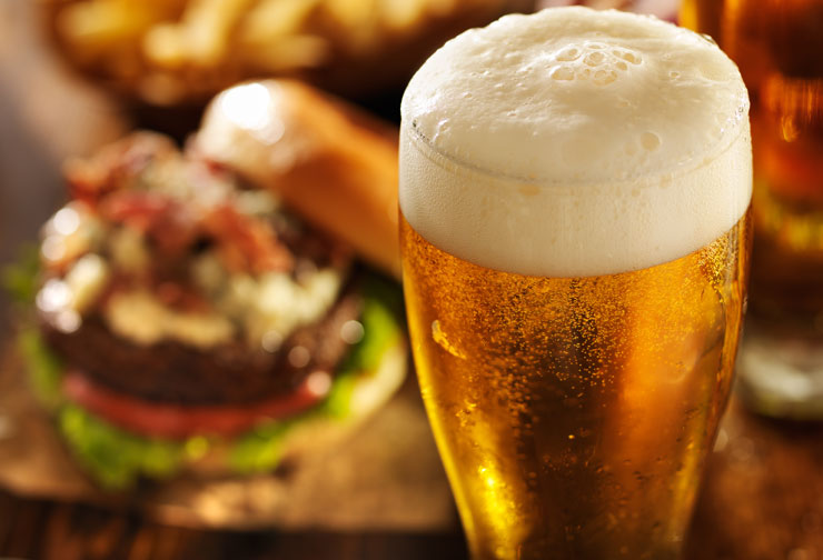 a glass of beer with a head of foam and a hamburger on a wooden table