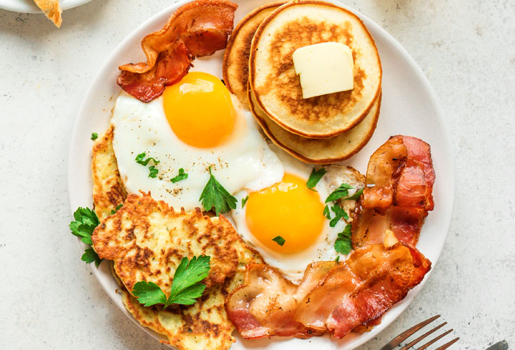 a typical American breakfast plate of eggs, bacon, pancakes, and hash browns