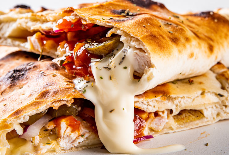 a close-up of a calzone filled with ricotta cheese, mozzarella cheese, and ham.