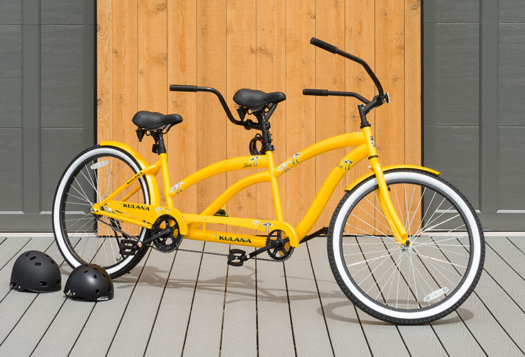 Stylish Tandem bicycle with yellow body and black seats with two helmets on a deck