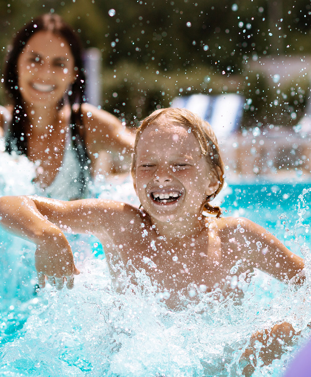Boy in pool splashing water with mom in background