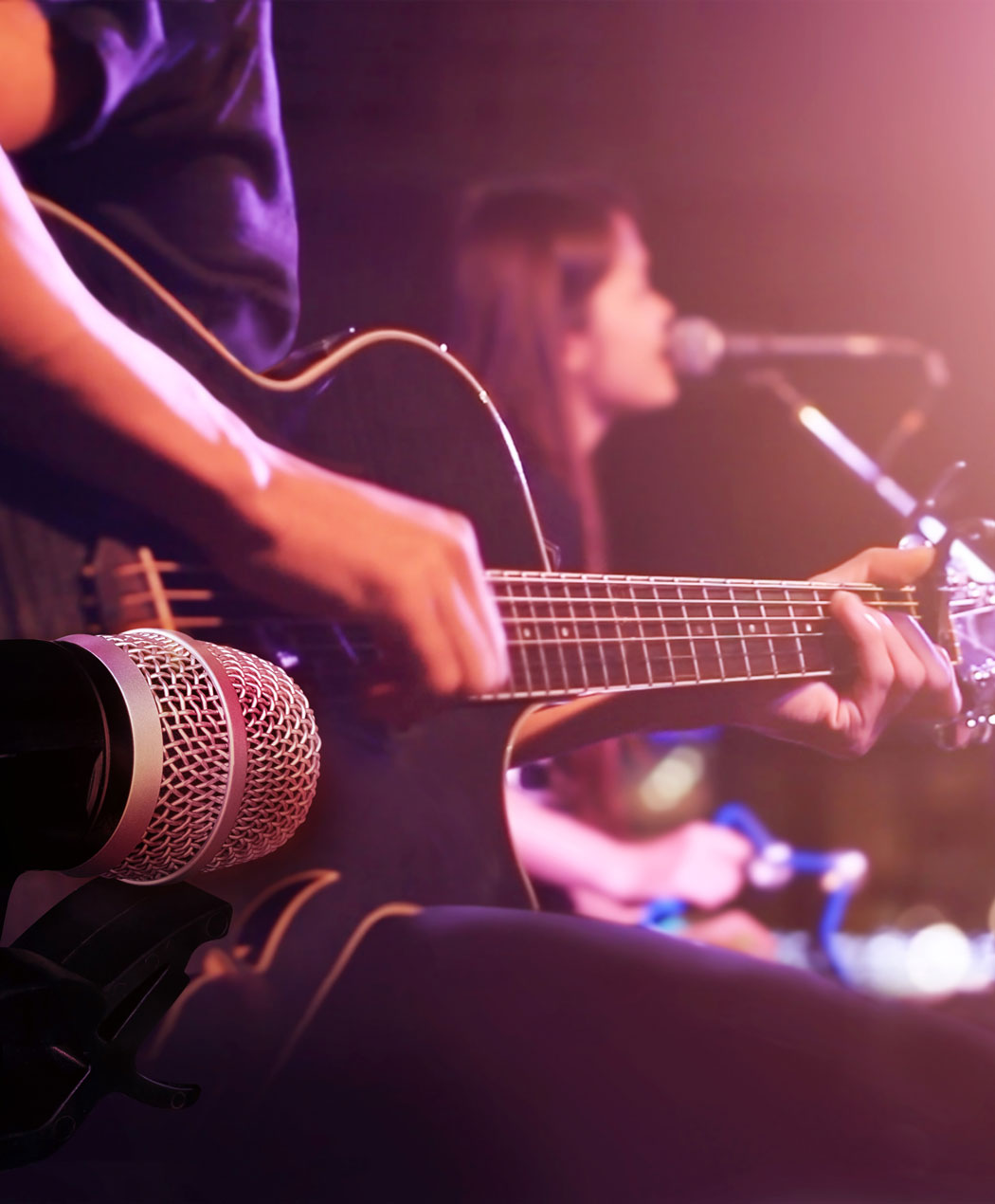 close up view of man playing guitar with woman singing into microphone in the background