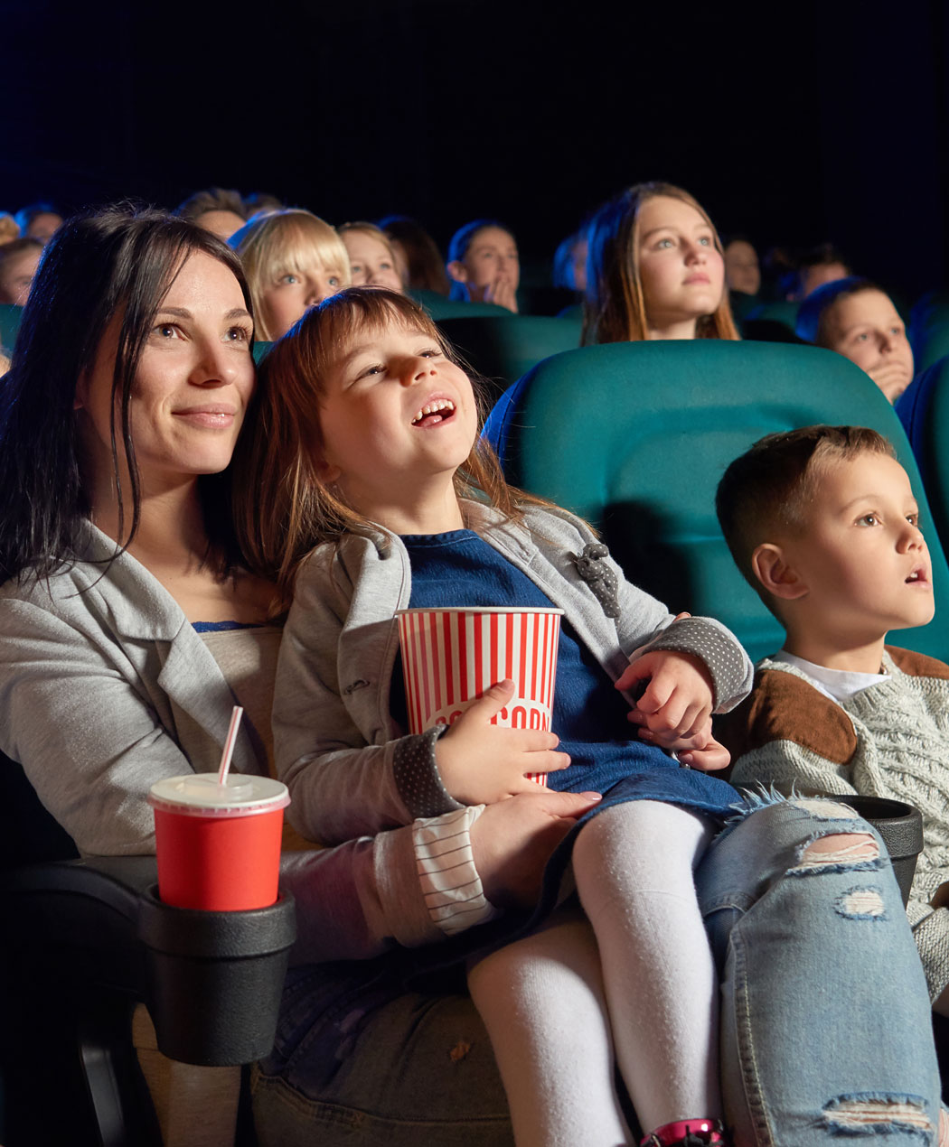 mother holding daughter in arms next to young boy in movie theater watching a movie