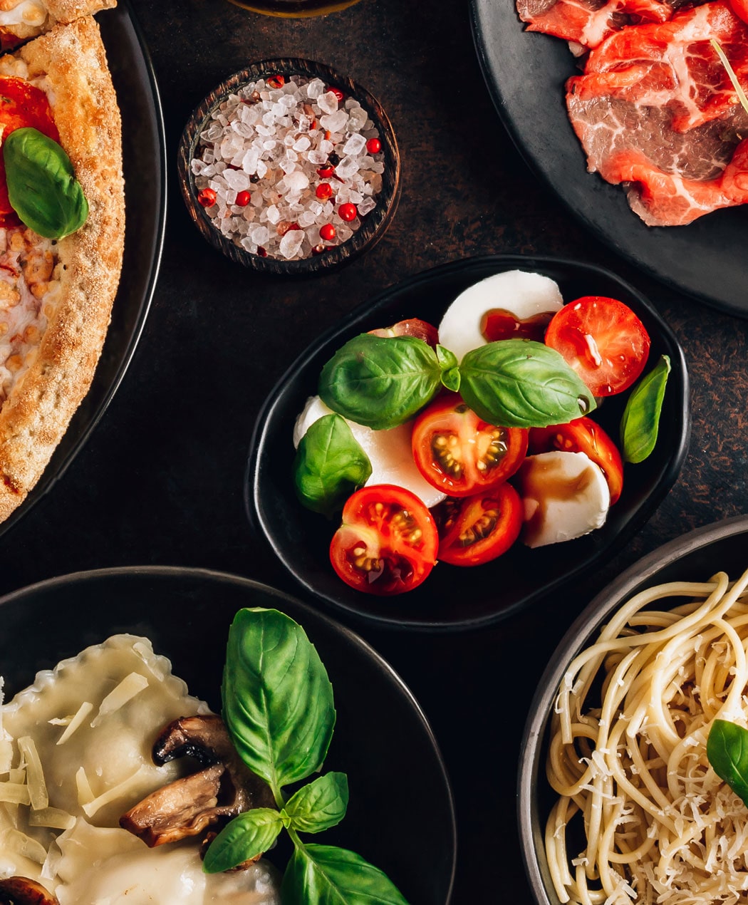 bowl of caprese salad, spagetti, ravioli and pizza crust