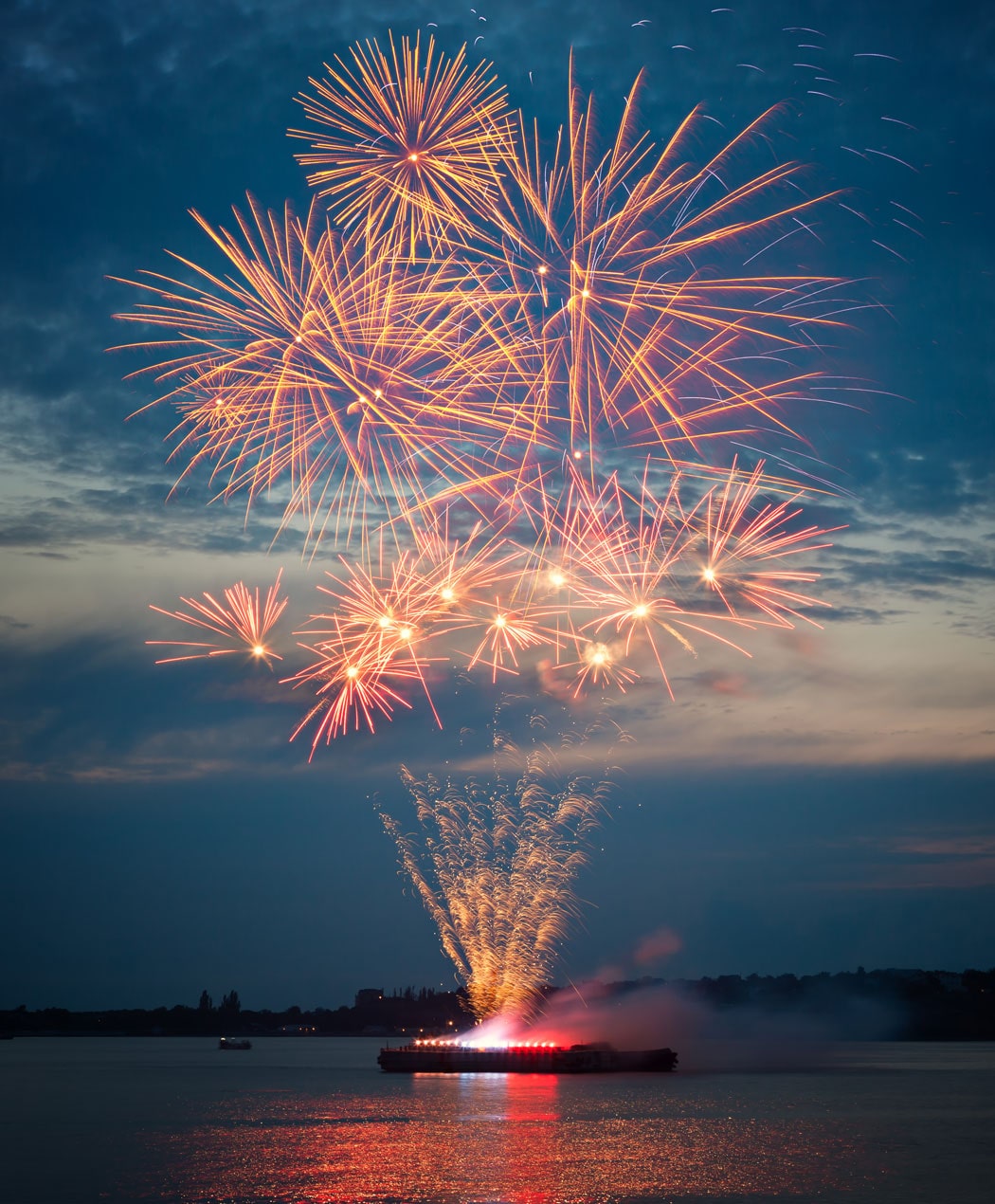 red fireworks in the distance over a lake at dusk