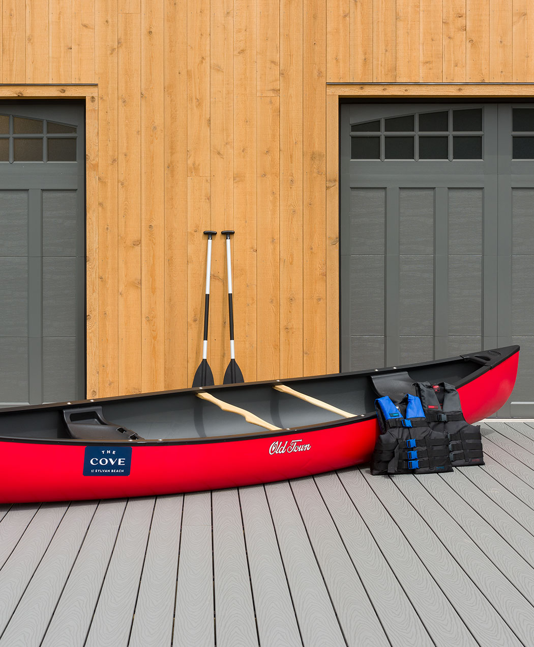 Red canoe with two paddles and two life jackets on a deck