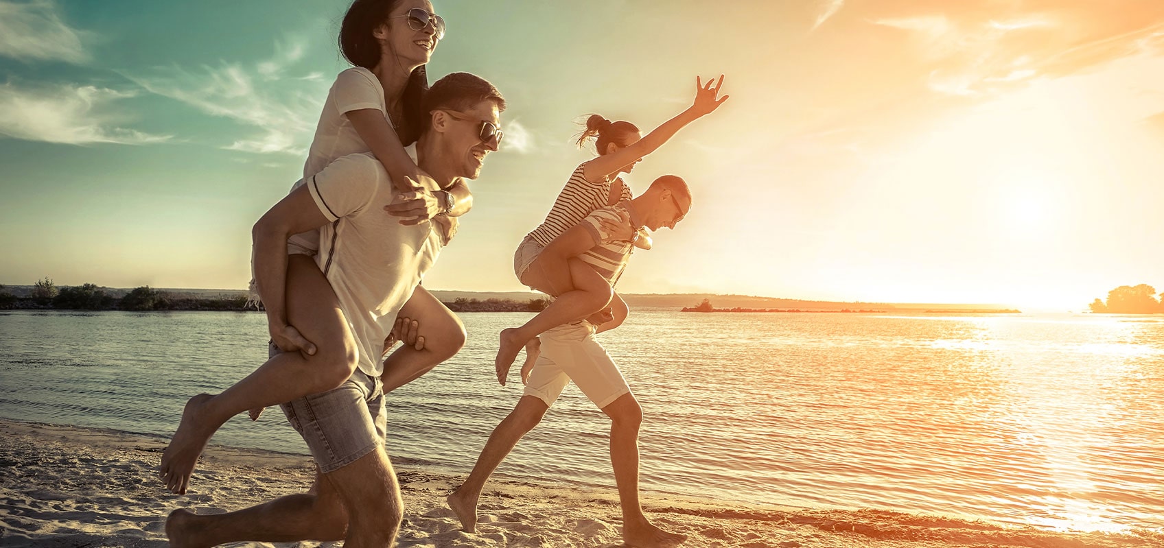 Two men piggybacking female friends at the beach