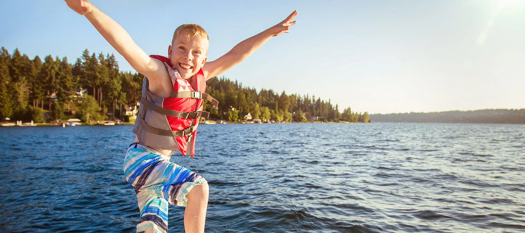 Boy wearing life jacket jumping into a lake